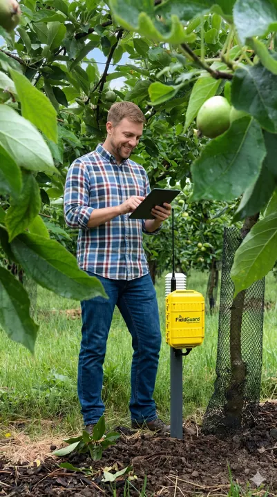 Fruitteler bekijkt TRACIS-data op een tablet naast een FieldGuard meetstation in de boomgaard